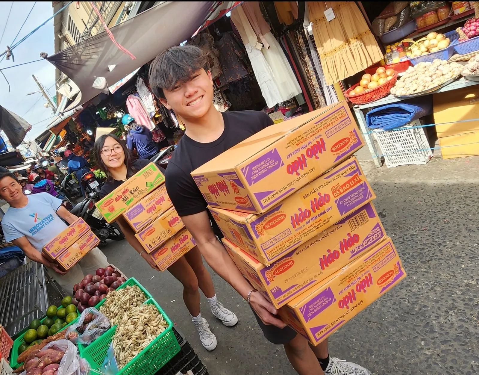 Rilina and Dylan carry cases of food through a market